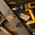 Gros plan sur divers outils, dont une perceuse, un marteau et un pinceau, posés sur un établi en bois.