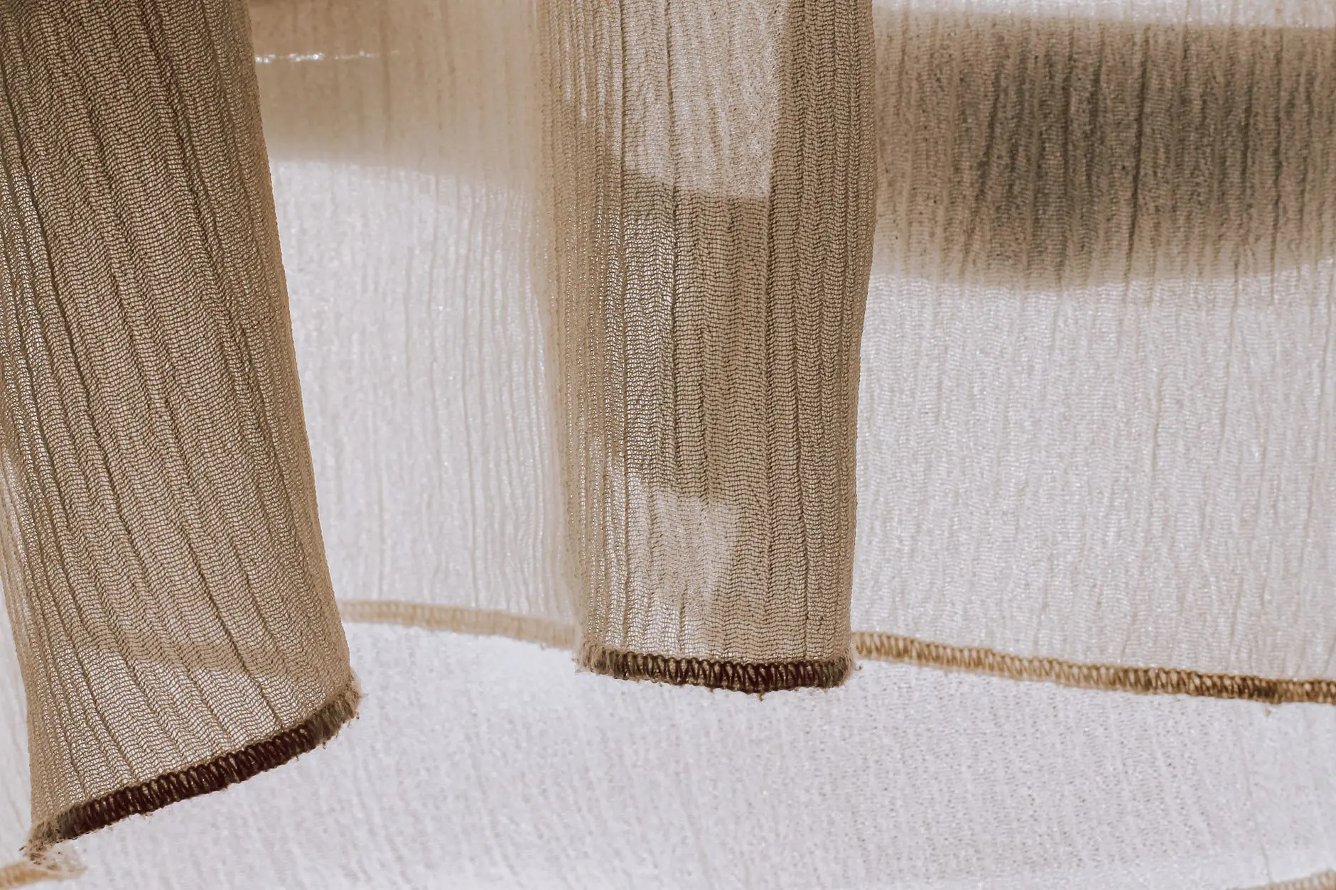 Gros plan sur un tissu transparent où la lumière du soleil crée des ombres et des textures délicates, parfait pour le design textile.